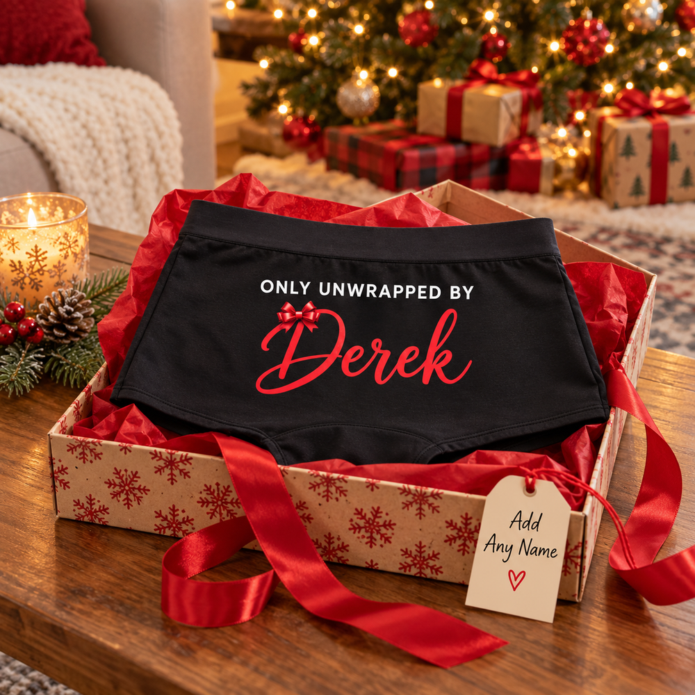 Only Unwrapped By custom name boyshort panties in a snowflake gift box with red tissue by a Christmas tree, with an Add Any Name tag