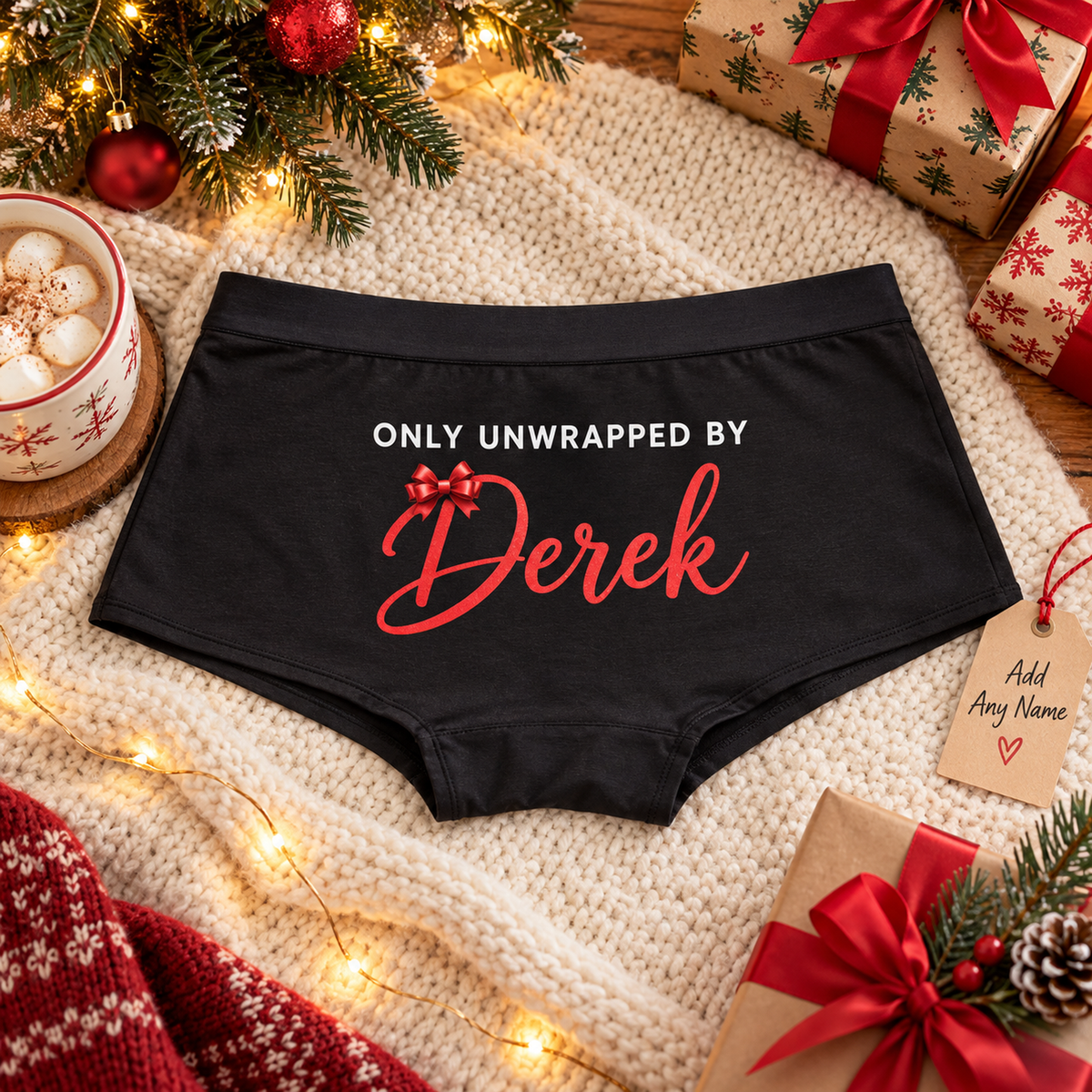 Personalized black boyshort panties printed “Only Unwrapped By Derek” in white caps and red script with a red bow, on a knit blanket with Christmas gifts (any name can be added)