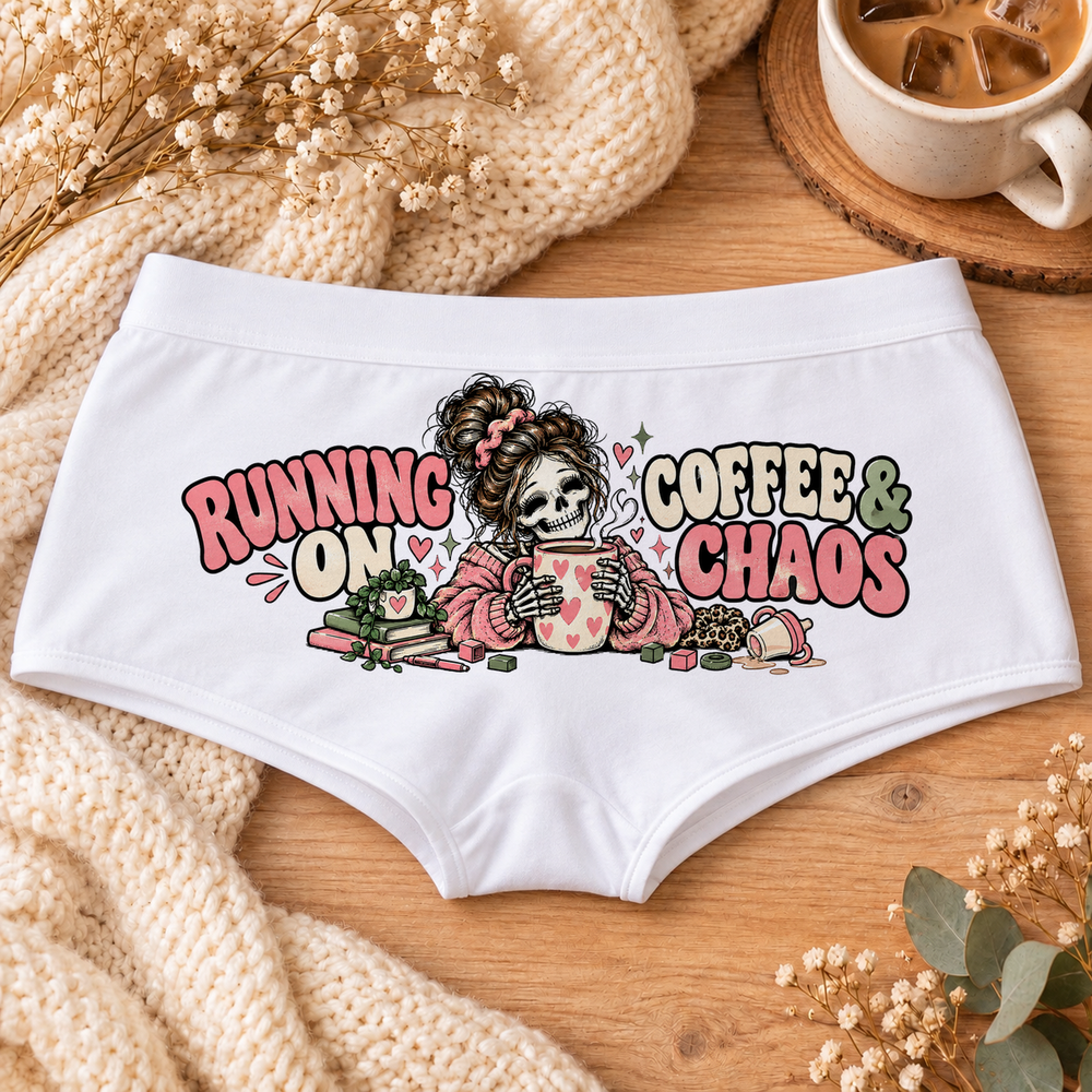 White Running on Coffee & Chaos tired mom boyshort underwear with a messy-bun skeleton mom holding a heart coffee mug, pink and sage lettering, flat-lay